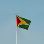 A vibrant Guyana national flag waving on a flagpole against a clear blue sky in Georgetown, Guyana.