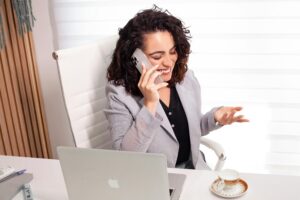 Smiling woman in office on phone, maintaining business communications with technology.