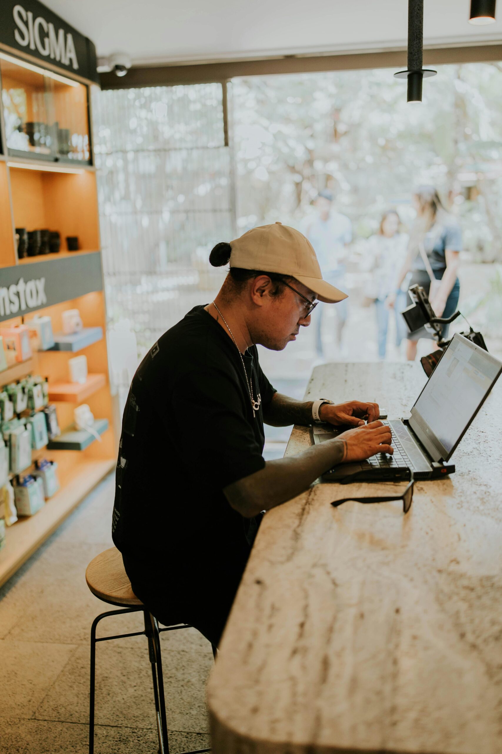 Casually dressed man focuses on his laptop at a cafe counter, surrounded by Polaroid cameras.
