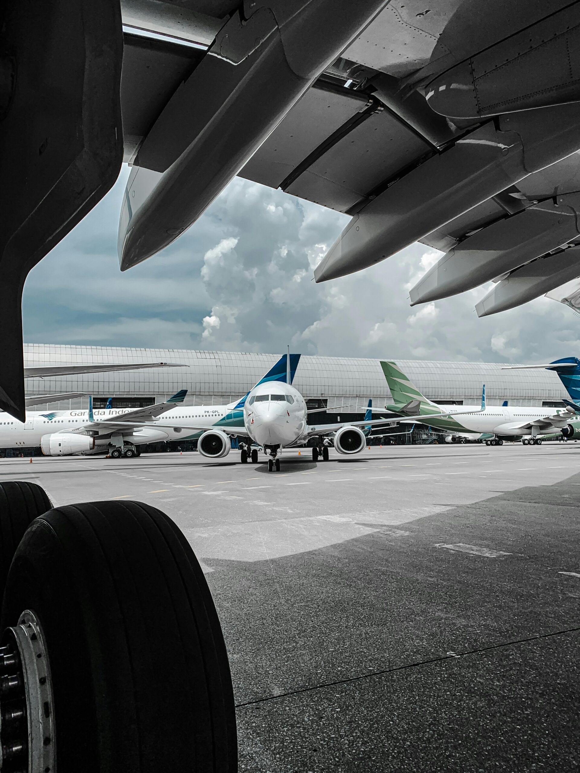 Several airplanes are parked on the airport tarmac under a cloudy sky, awaiting their next flights.